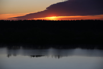 Dramatic sky background.The Golden light of the rising sun at dusk illuminates the overhanging continuous cloud on the clear horizon and the forest reflected in the ripples of a calm lake.Russia