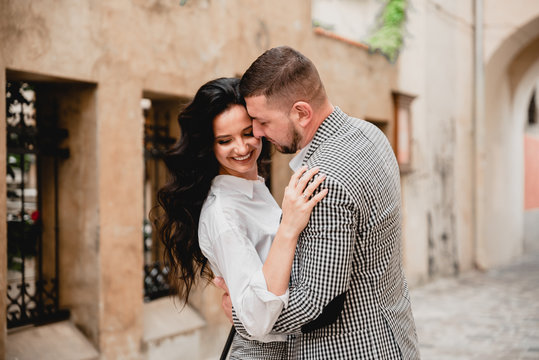 Charming girl with long brown hair and a man with a beard kissing on the background of the morning city. Newlyweds on their wedding day