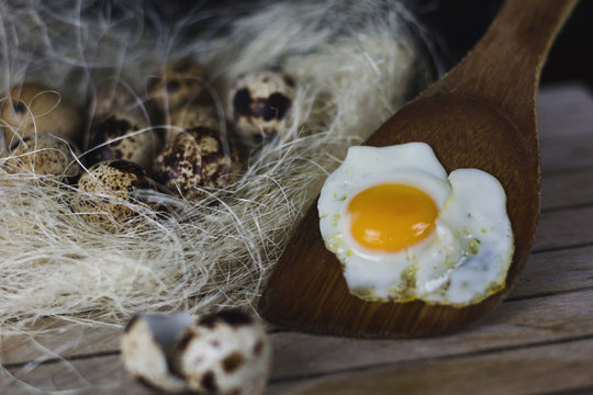 Nido de paja y heno con huevos de codorniz, huevo frito sobre cuchara de madera y cascara de huevos  sobre palet de madera