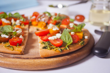 Homemade pizza with cherry tomatoes, fresh green basil and feta cheese. Homemade food. Concept for a tasty and hearty meal. Wooden background. Close up.