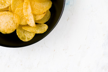 black plate filled with potatos chips on a white wooden background. Unhealthy concept