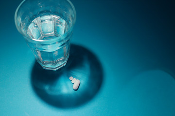 foto horizontal con vaso de agua proyectando sombras y  pastillas 