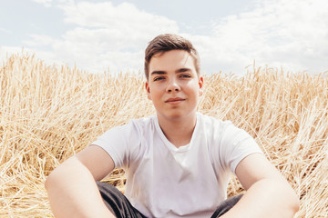 Portrait of smiling handsome teenage boy outdoors, in front of wheat field, at summer day.