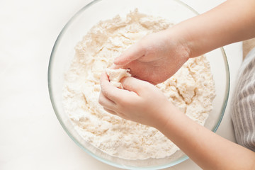Little child in the home kitchen preparing dough for pizza or another food. Top view.