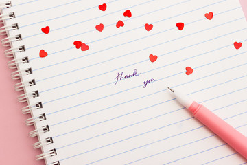 Thank you words written by hand on a lined notebook decorated with red confetti hearts....