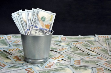 A bucket of dollars оn a background of pile of hundred-dollar bills. The concept of wealth and...