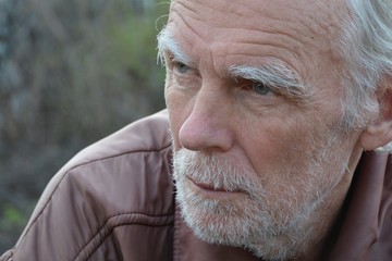 Portrait of an old gray haired unshaven man with a thoughtful look close up