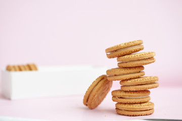 round homemade cookies stacked in a stack in a white box with vanilla cream on a light pink background.
