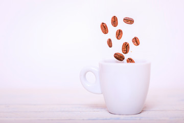 Roasted coffee beans falling into coffee cup on saucer with white background, fresh and bright wallpaper concept. Coffee beans falling in white cup. Highspeed shot.