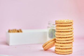 round homemade cookies stacked in a stack in a white box with vanilla cream on a light pink background.