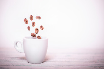 Roasted coffee beans falling into coffee cup on saucer with white background, fresh and bright wallpaper concept. Coffee beans falling in white cup. Highspeed shot.