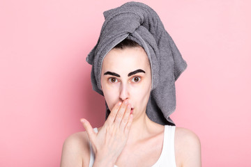 Young woman with towel on her head paints her eyebrows on her own. From surprise covers his mouth...