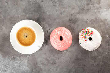 White cup of coffee and two donuts in white and pink icing on grey background. Flat lay