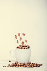 Coffee beans falling in white cup. Highspeed shot. Roasted coffee beans falling into coffee cup on saucer with white background, fresh energy wallpaper concept.
