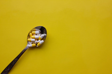 Yellow and white capsules and white pills in a spoon on a yellow background