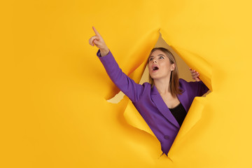 Pointing, showing. Cheerful caucasian young woman poses in torn yellow paper background, emotional...