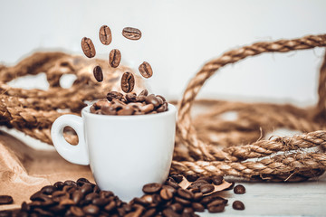 Roasted coffee beans falling into coffee cup with paper bag and scoop on old rusty background. Fresh energy wallpaper concept.