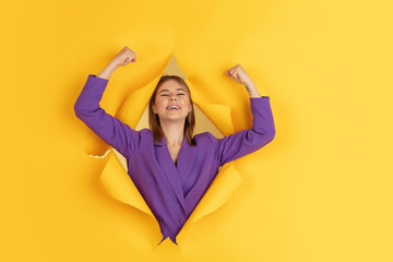 Happy winner. Cheerful caucasian young woman poses in torn yellow paper background, emotional and expressive. Breaking on, breakthrought. Concept of human emotions, facial expression, sales, ad.