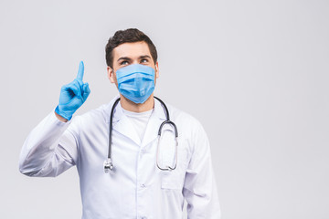 Doctor man in medical gown sterile face mask gloves isolated on white background. Epidemic pandemic coronavirus 2019-ncov sars covid-19 flu virus. Pointing finger aside up.