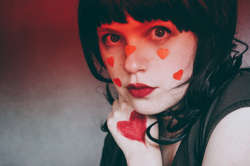 Artistic portrait of a young woman with red heart make up and covering by a red gradient ligth