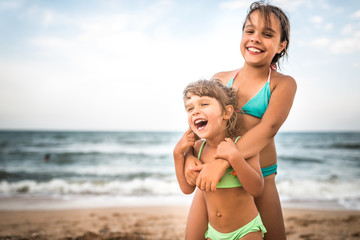 Two cute positive little girls sisters raised their hands up while swimming at sea during the holidays on a warm summer day. Concept of healthy and joyful children