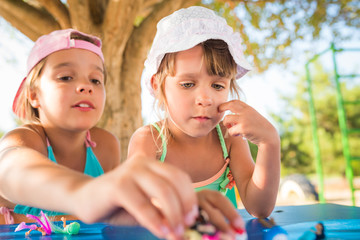 Two little cute girls playing dolls outdoors while relaxing on the beach on a hot summer day. The concept of active games for children.