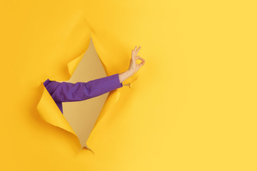Showing nice. Female hand gesturing in torn yellow paper hole background. Breaking on, breakthrought. Concept of business, finance, shopping, proposal, sales, ad. Copyspace. Promotions discounts
