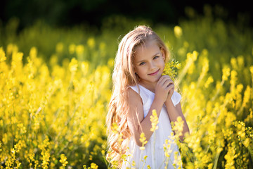 Portrait of a cute happy little girl 5-7 years old in nature, in the summer in a rape field.