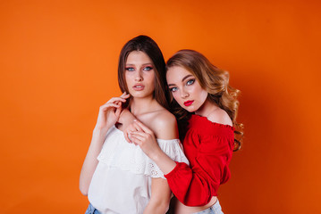 Two young and beautiful girls shows emotions and smiles in the Studio on an orange background. Girls for advertising