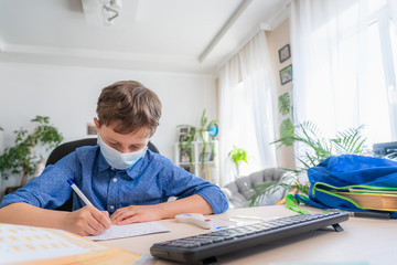 boy in face mask using computer, doing homework during coronavirus quarantine