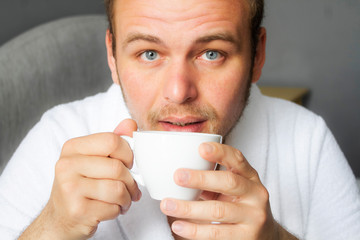 Closeup photo of a young man with a cup of coffee. Morning coffee. Breakfast in bed.