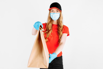 Courier in uniform, with a medical mask on his face and gloves holding a paper bag with food on a white background. The concept of shipping, quarantine, coronavirus