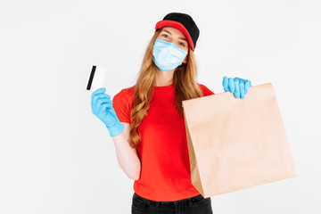 Fototapeta na wymiar A courier, wearing medical rubber gloves and a medical mask, standing with a paper bag and a credit card on a white background. Online stores, payment by Bank transfer, quarantine, coronavirus