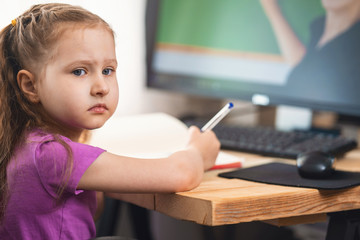 cute little girl using a computer for remote e-learning rubs her eyes