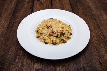 Italian risotto with porcini mushrooms and bacon in a white plate on a wooden table.