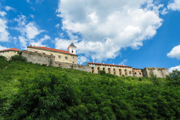 Fototapeta na wymiar Mukachevo castle in sunny weather on a hill. Memos of architecture. The remains of forteci in the city of Mukachevo. Harmonious sky and sunny weather in Transcarpathia. Hill with green trees. Ruin.