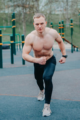Obraz premium A young guy stretches and warms up on the sports ground. Athlete man in running pose on city street. Sport tight clothes. Bright sunset. sport man on starting position 20-30s