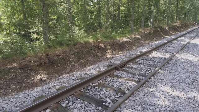 AERIAL DRONE CLOSE FORWARD SIDE MOVEMENT OF RAILWAY TRACKS IN GREEN WOODS