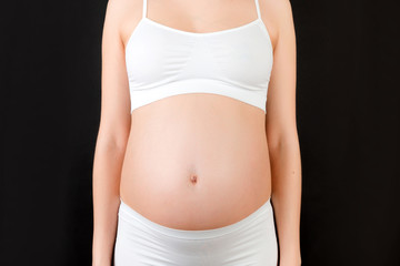Cropped image of pregnant woman's belly at black background. Future mom in white underwear. Parenthood concept. Copy space