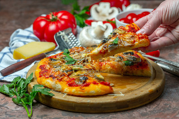 Hand with a slice of pizza with mushrooms and tomatoes.