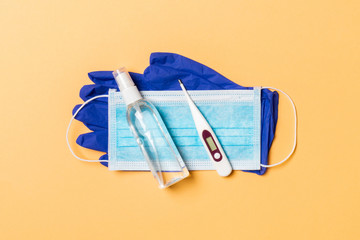 Top view of latex gloves, bottle of alcohol hand sanitizes, medical mask and digital thermometer on orange background. Antibacterial virus protection concept with copy space