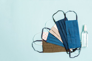 Top view of personal protection such as a pile of homemade textile masks and alcohol hand sanitizer on blue background. Health care concept with copy space