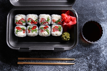 Set of delicious sushi rolls with wassabi and ginger in a box. Wooden chopsticks and soy sauce on a dark background. Top view. Japanese food.