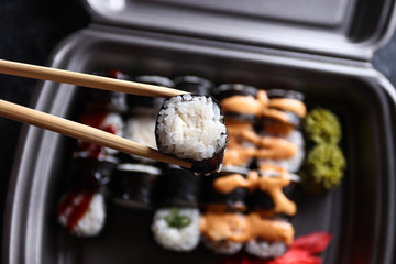 Set of delicious sushi rolls with wassabi and ginger in a box. Sushi rolls hold with wooden chopsticks. Top view. Japanese food.