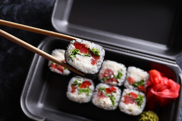 Set of delicious sushi rolls with wassabi and ginger in a box. Sushi rolls hold with wooden chopsticks. Top view. Japanese food.