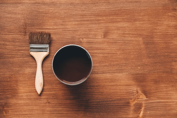 Open jar of brown paint with a brush on wooden background. Repairing concept. Top view. Copy, empty space for text