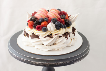 Pavlova cake with whipped cream, raspberry, blueberry, blackberry and french macaroons. Copy space, plain background.