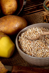 barley on wooden spoons, dried plums next to one peeled potato and dried mushrooms next to dried spices