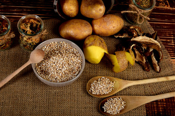 barley on wooden spoons, dried plums next to one peeled potato and dried mushrooms next to dried spices