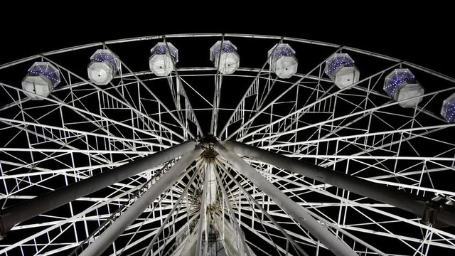 4K: Ferris Wheel lit up at night in the dark evening skay. The big round circle rotates and is illuminated. Underneath. Stock Video Clip Footage